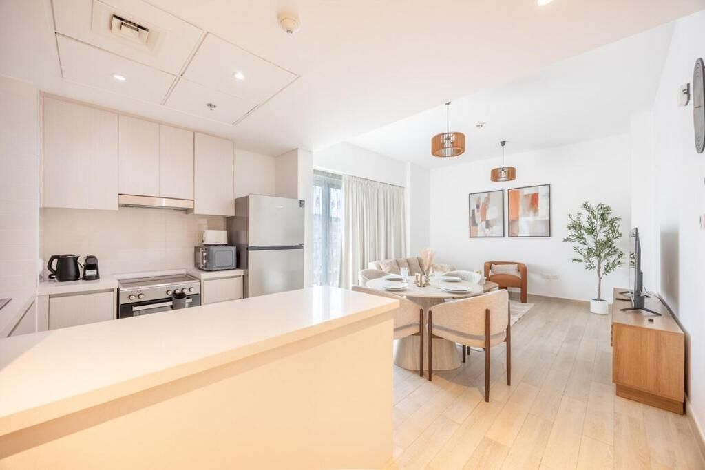 A modern kitchen with white cabinets, a central island, and a dining area with a round table and chairs.