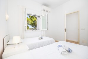 Et hotelværelse med to senge, et vindue med gardiner, et sengebord med en lampe og en dør.