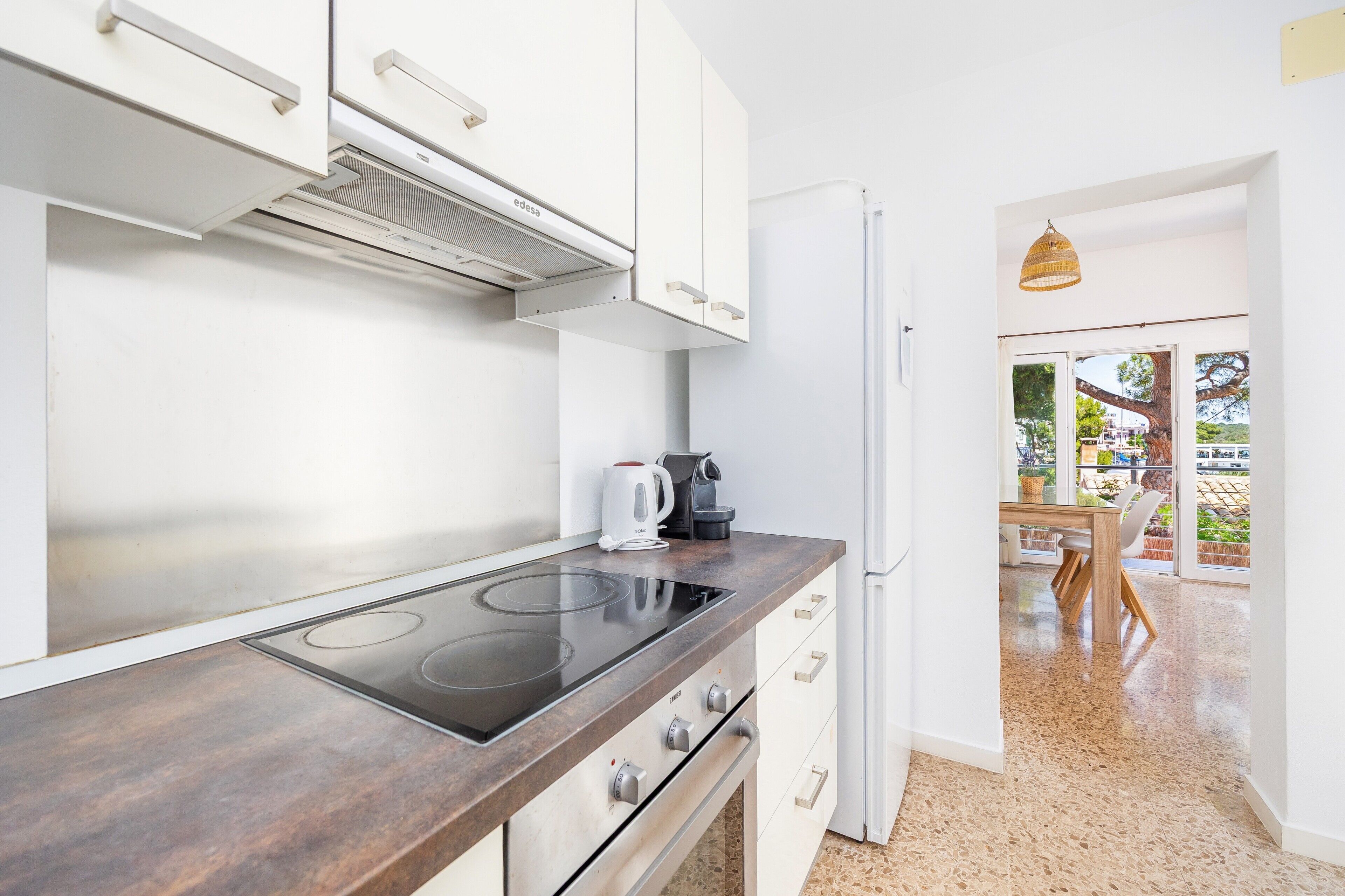 Una cocina moderna con estufa integrada, armarios blancos y un refrigerador.