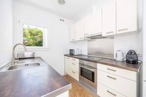 Une cuisine moderne dotée d’appareils électroménagers en acier inoxydable, d’une fenêtre donnant sur un espace verdoyant et d’un plan de travail sur lequel se trouvent un grille-pain et une bouilloire.