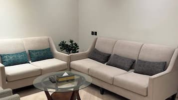 Ein Wohnzimmer mit zwei Sofas, einem Glastisch und einem Blumentopf.