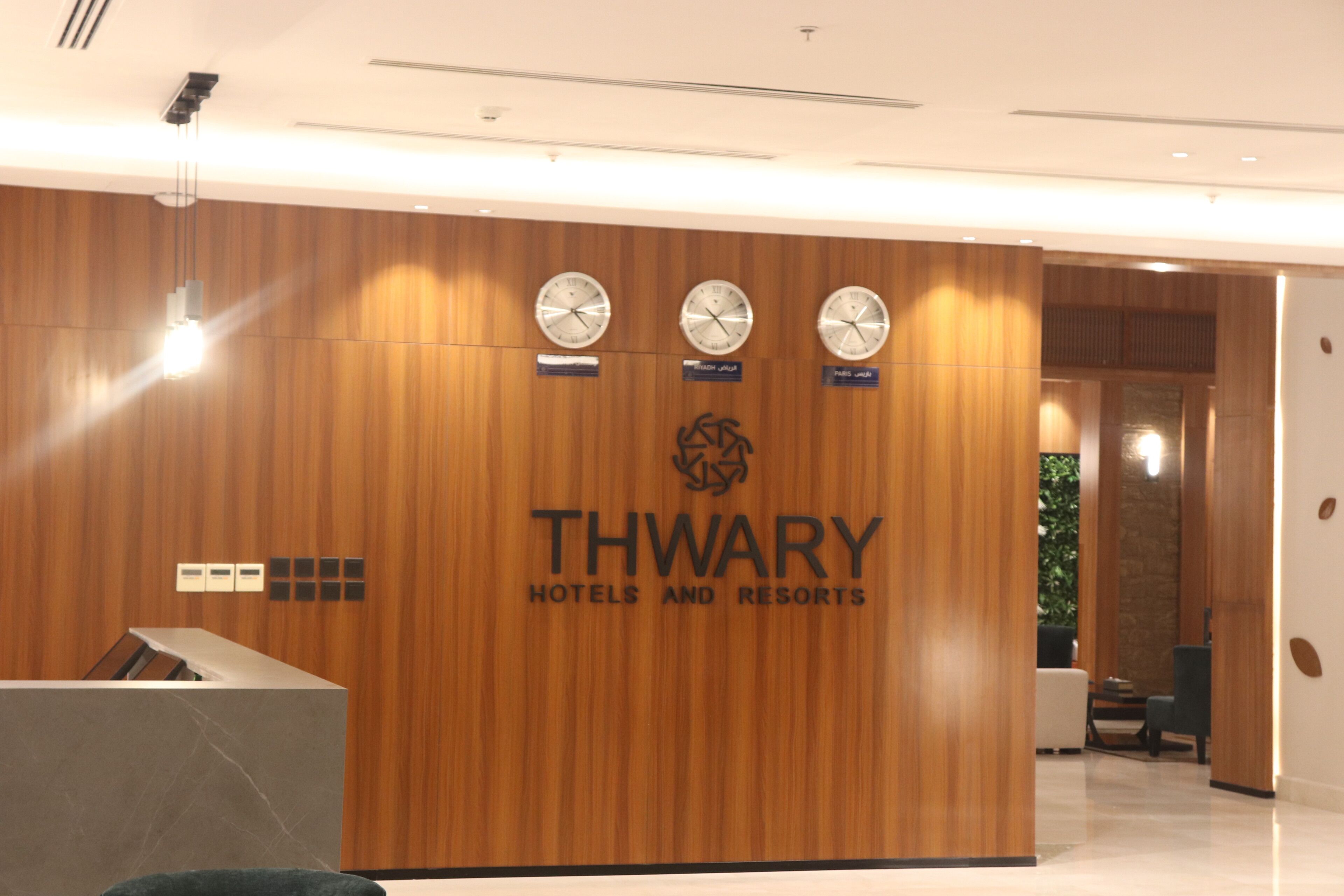 A reception desk with a wooden panel wall, three clocks, and a logo for THWARY HOTELS AND RESORTS.