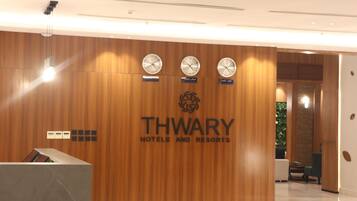 A reception desk with a wooden panel wall, three clocks, and a logo for THWARY HOTELS AND RESORTS.