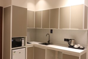 A compact kitchenette with a microwave, a kettle, and a sink. - Thawari Hotel Apartments (Riyadh)