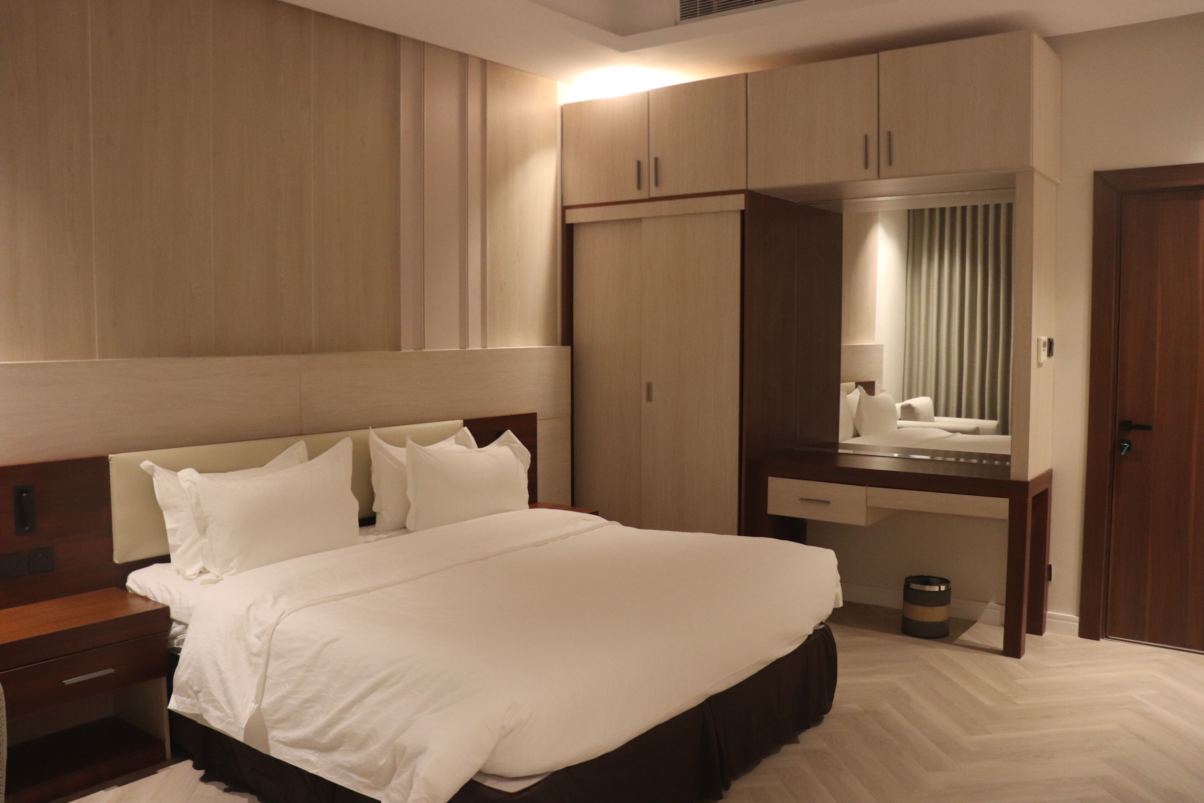 Een hotelkamer met een groot bed, een bureau met spiegel en een kledingkast.