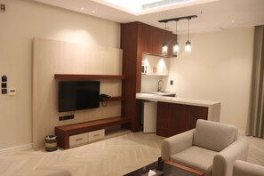 A modern living room with a flat-screen TV, wooden entertainment unit, and a sofa. - Thawari Hotel Apartments (Riyadh)