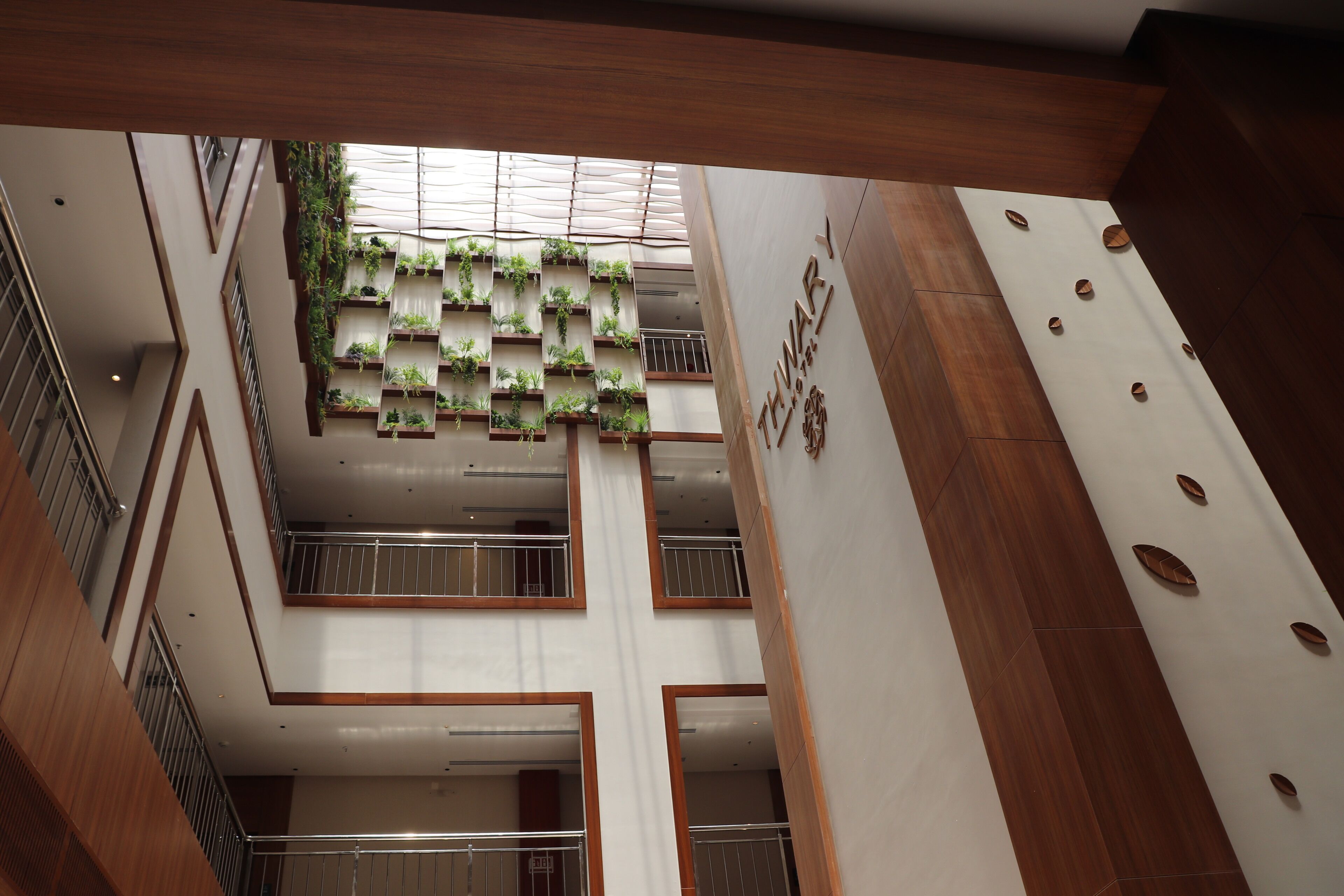 A multi-level interior with a central atrium featuring a vertical garden, wooden paneling, and a sign indicating a hotel.