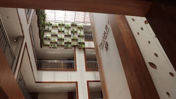 A multi-level interior with a central atrium featuring a vertical garden, wooden paneling, and a sign indicating a hotel.