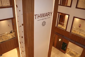 Een THWARY HOTEL bord met een logo, gelegen in een gebouw met meerdere verdiepingen, houten lambrisering en een glazen balustrade.