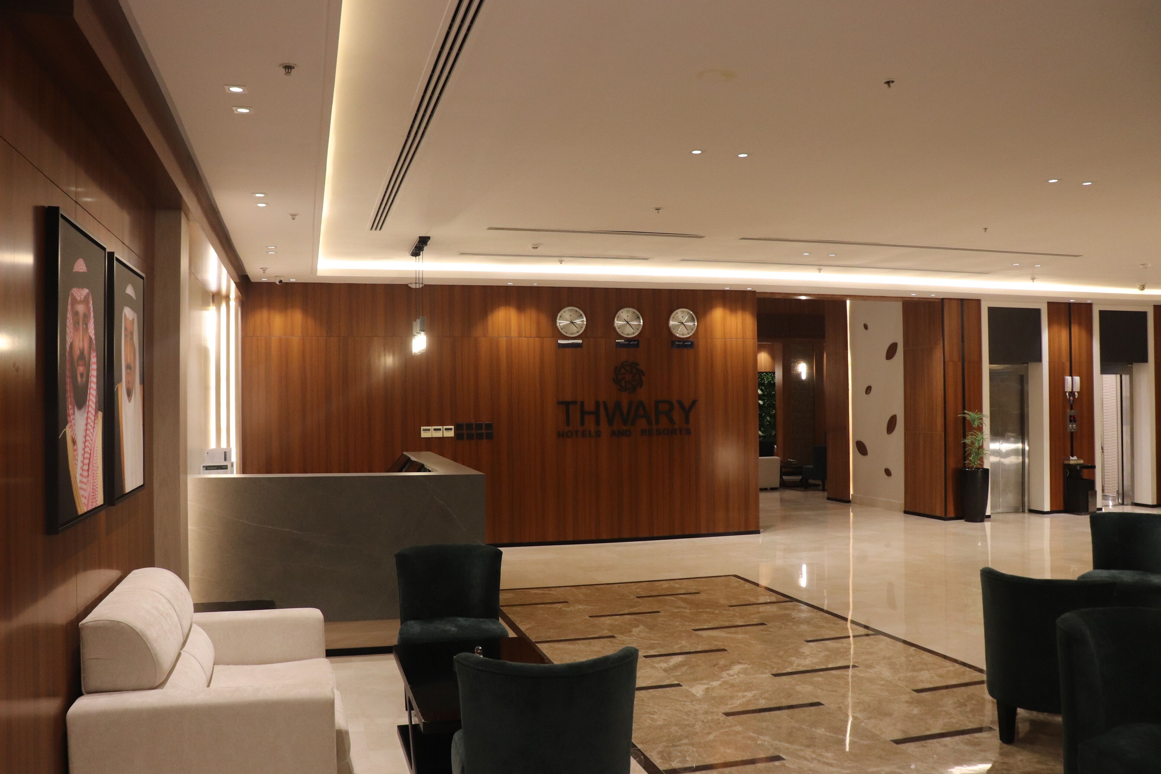 Een moderne hotel lobby met een receptiebalie, een zithoek en een klok aan de muur.