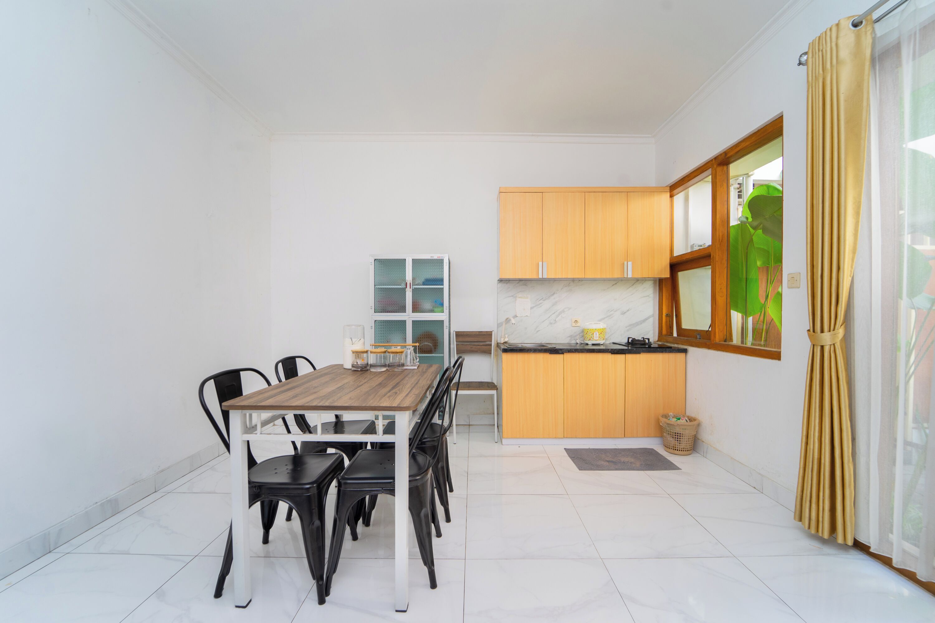 A compact kitchen with wooden cabinets, a marble countertop, and a dining area with a wooden table and black chairs.
