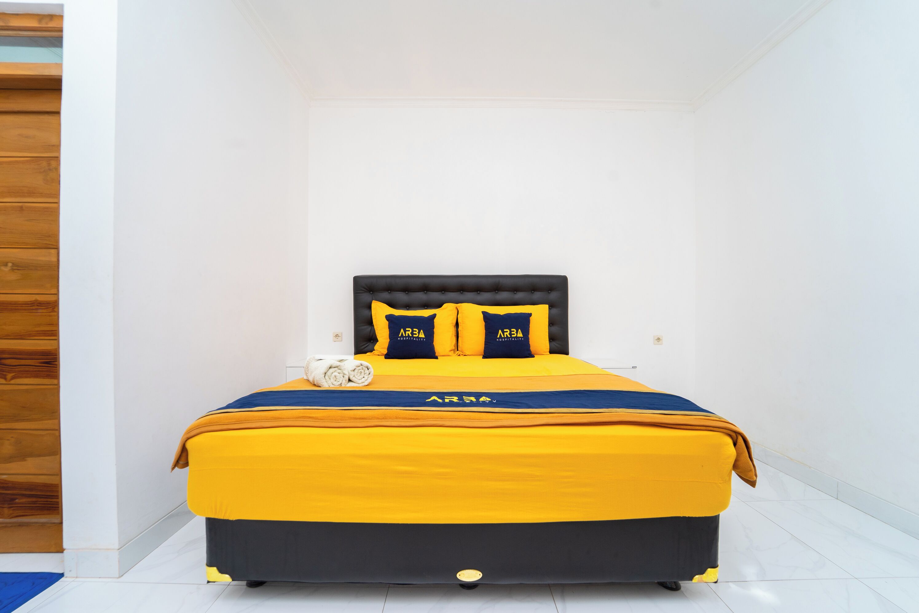 A neatly made bed with a black headboard and yellow bedding, featuring the brand name 'AREA' on the pillows and bedspread.
