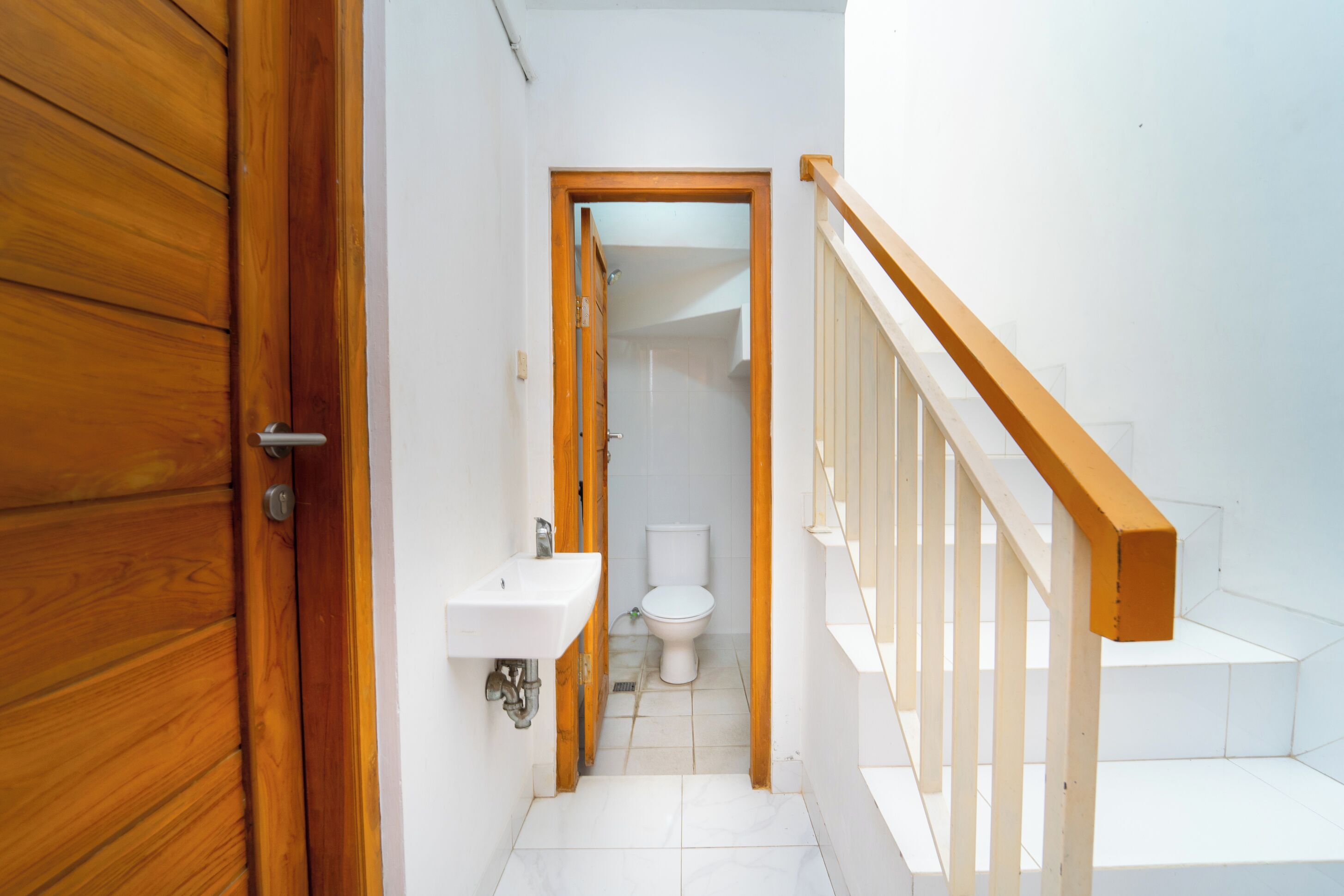 A narrow hallway with a wooden door on the left, a white sink, and a toilet in the center.