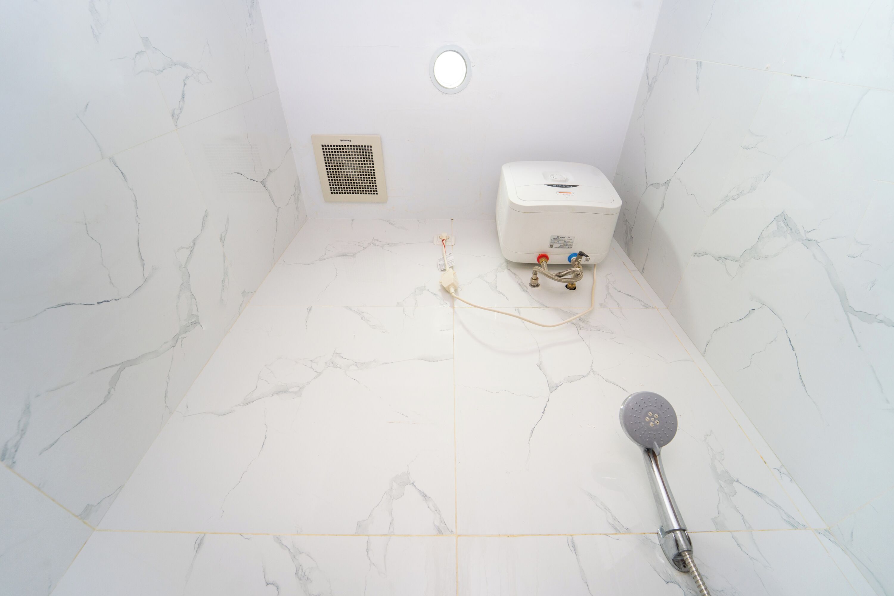 A bathroom with white marble tiles, a showerhead, a toilet, and a ventilation unit.