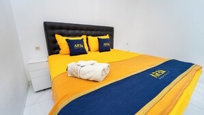 A hotel room with a bed featuring a yellow and blue bedspread, two pillows with the hotel's logo, and a neatly folded white towel. - Griya Asy-Syifa Homestay by ARBA (Yogyakarta)