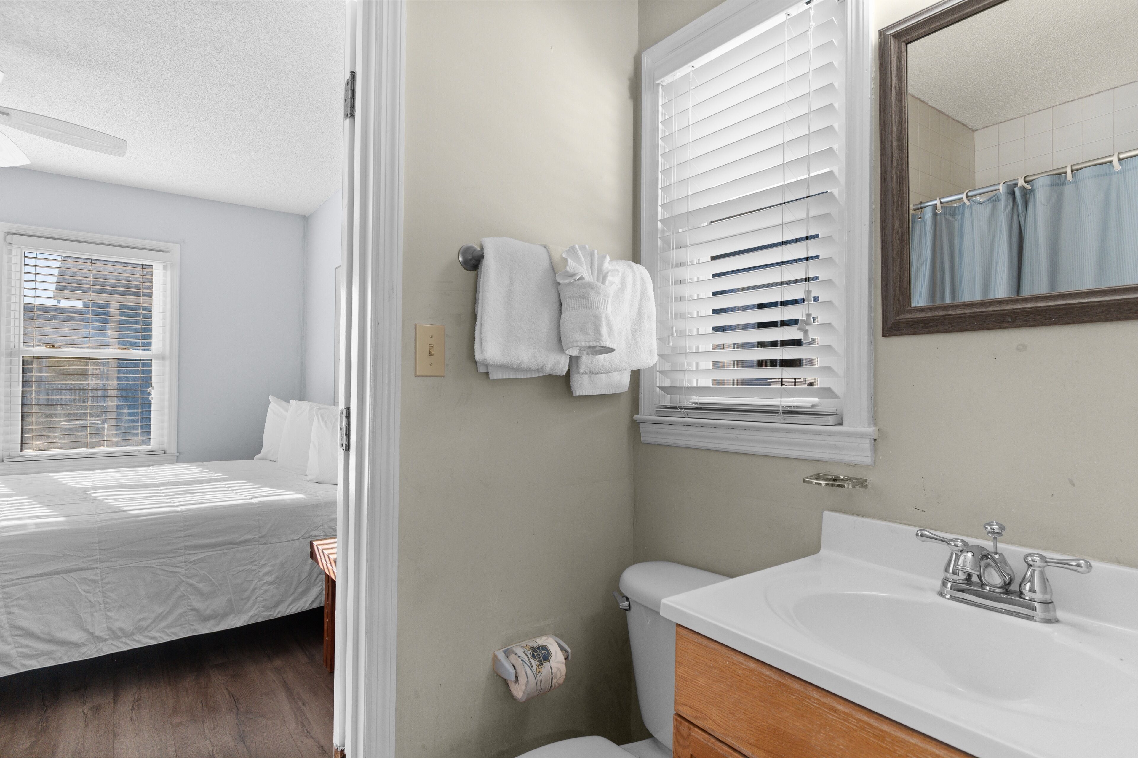 Ein Schlafzimmer mit Bett, ein Badezimmer mit Waschbecken und Toilette sowie ein Fenster mit Jalousien.