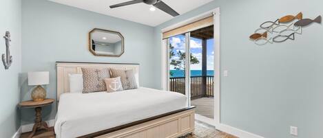 A bedroom with a bed, ceiling fan, and a view of the ocean through a sliding door.