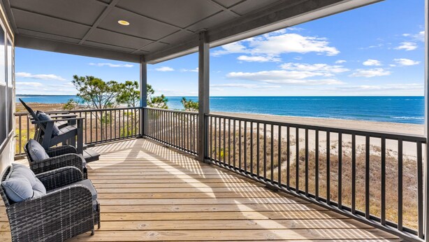 A covered deck with a view of the ocean, a railing, and wicker furniture. - Pet Friendly Beach House - Seminole Wind (Port St. Joe)