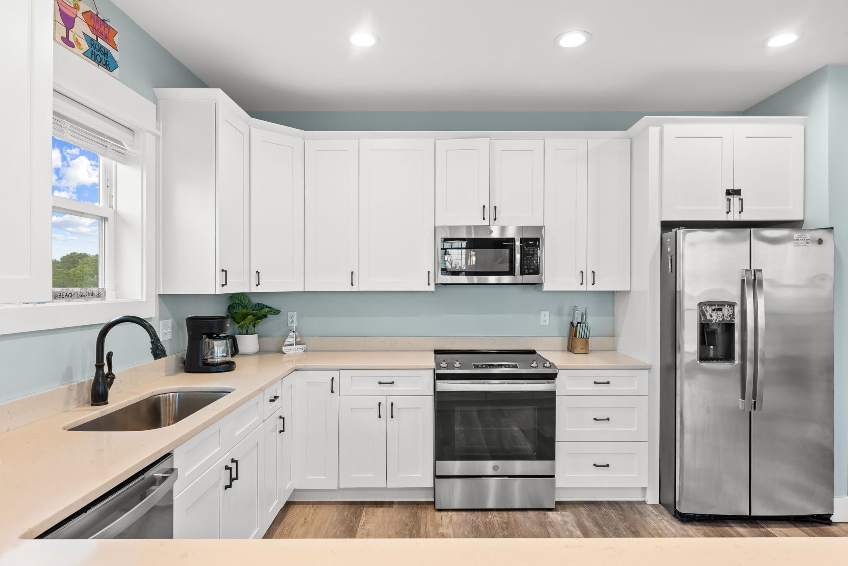 A modern kitchen with white cabinets, stainless steel appliances, a sink, and a window with a view.
