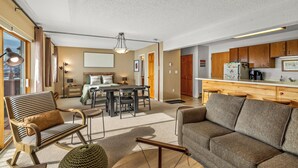 A spacious living area with a sofa, a dining table, and a kitchen area with wooden cabinets. - Cute, cozy studio at Storm Meadows~Ski In, Walk Out! (Steamboat Springs)