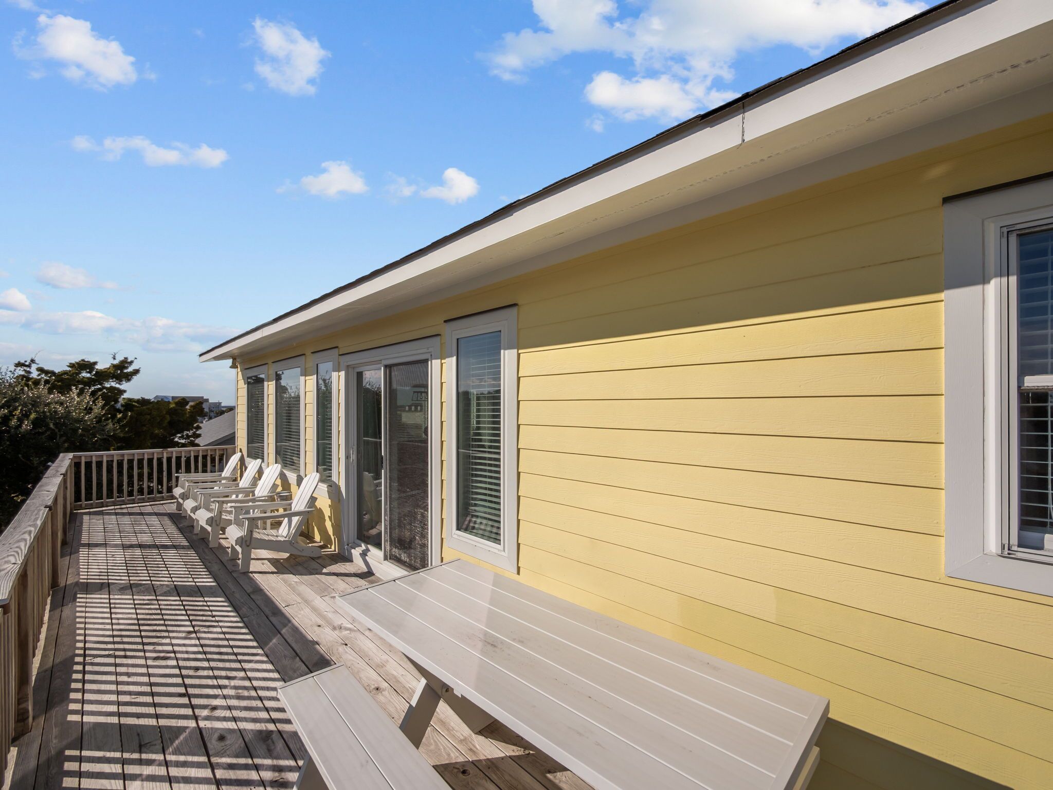 Un bâtiment jaune doté d’une terrasse couverte, de sièges en plein air et de grandes fenêtres.