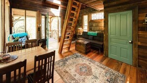 A wooden interior with a dining table, chairs, a sofa, a green door, and a ladder.