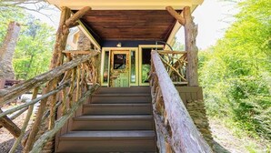 A wooden staircase leading to a covered entrance with a door, surrounded by trees.