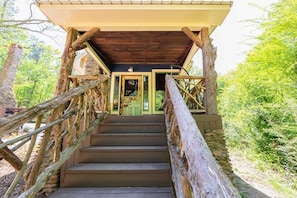 A wooden staircase leading to a covered entrance with a door, surrounded by trees.