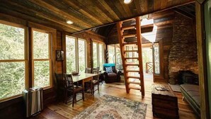 A rustic cabin interior with a dining area, a fireplace, and a stone wall.