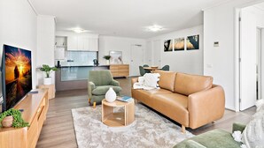 A modern living room with a leather sofa, a green armchair, and a TV. A kitchen is visible in the background. - Stylish Southbank Apartment With On-site Parking (Melbourne)