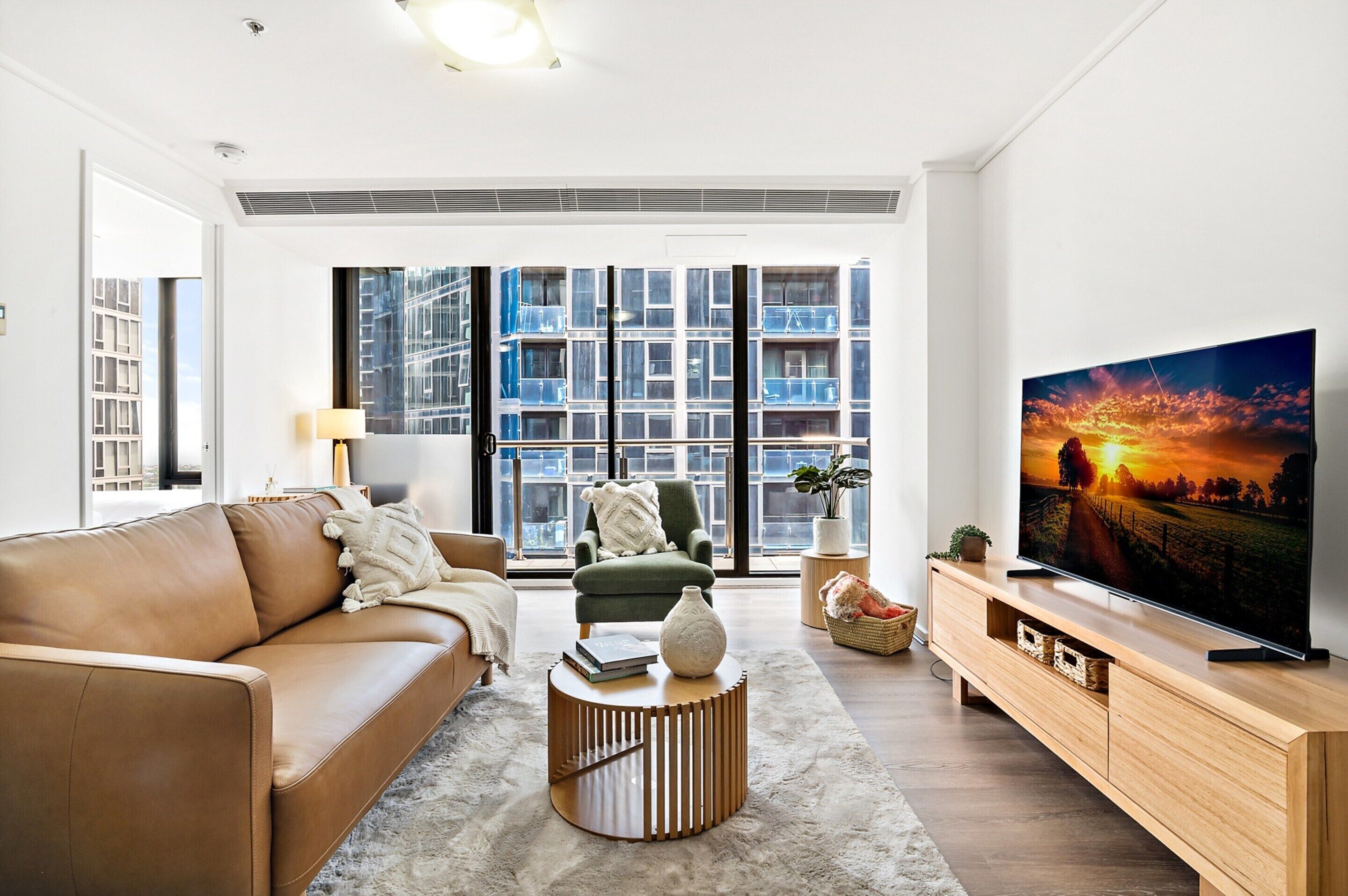 A modern living room with a leather sofa, a green armchair, a round coffee table, and a TV on a wooden stand.