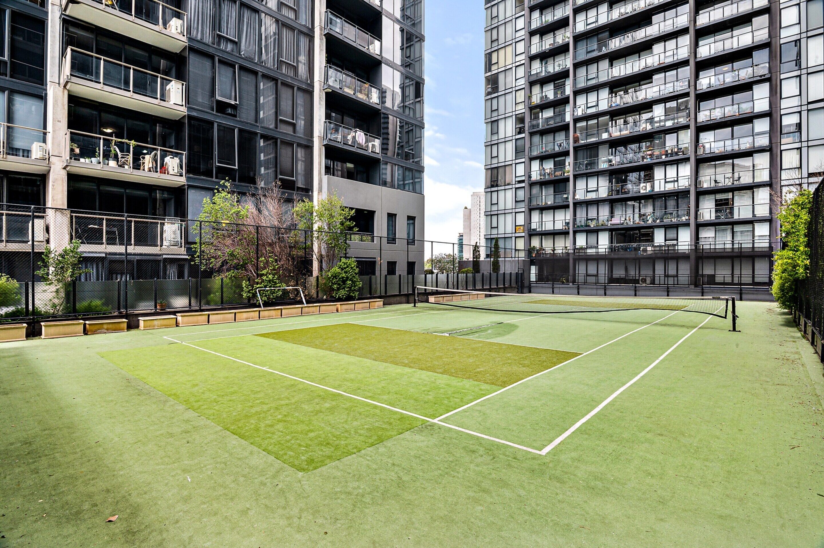 A tennis court with a net in the middle, surrounded by a fence.