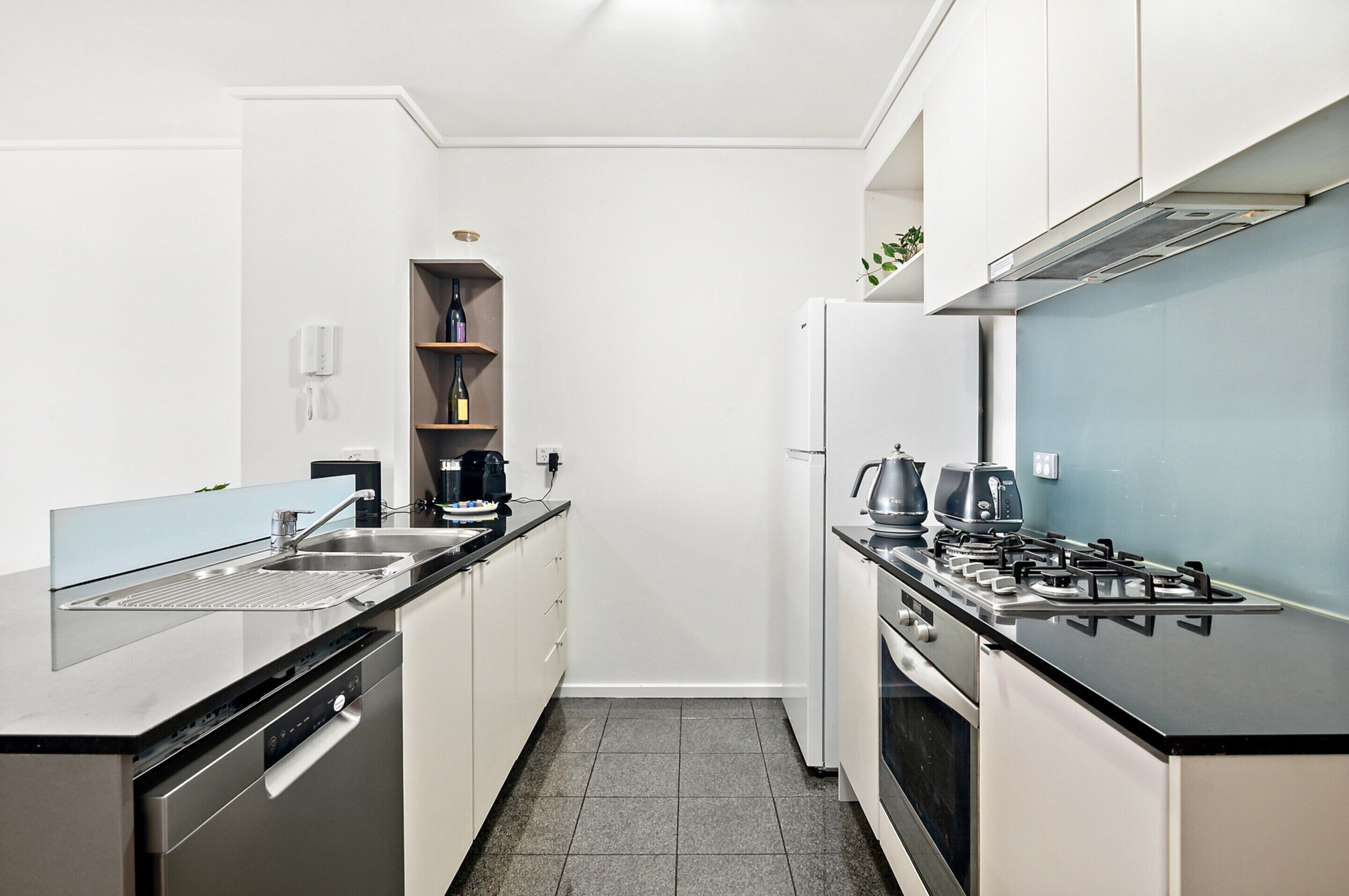 A modern kitchen with white cabinets, a black countertop, a built-in dishwasher, a stove, and a wine shelf.