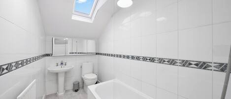 Et badeværelse med ovenlys, badekar, vask og toilet.