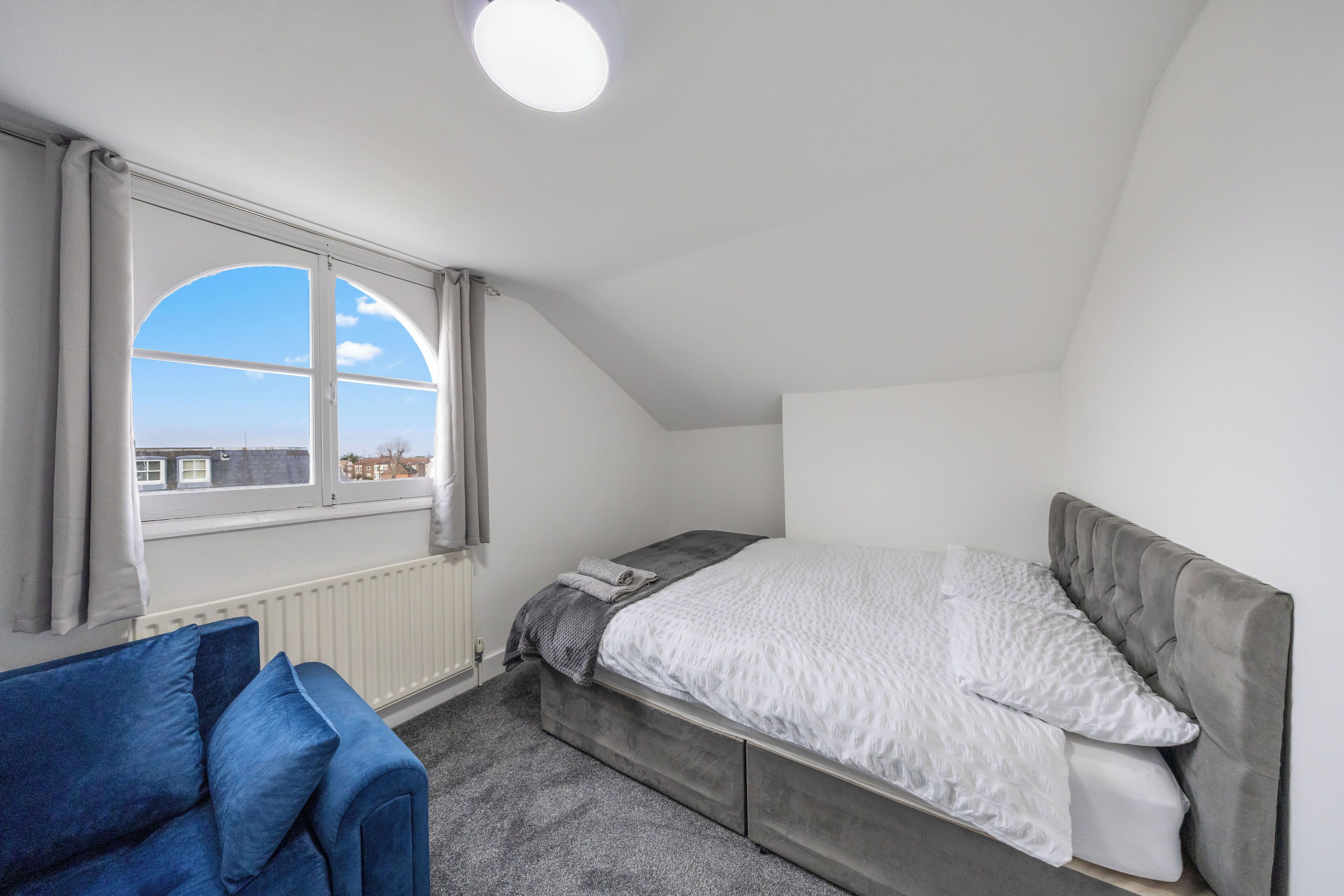 Ett sovrum med en säng, en blå soffa, ett fönster med gardiner och ett element.