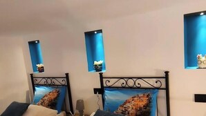 Une chambre d’hôtel avec deux lits simples, chacun agrémenté d’un oreiller bleu et d’une tête de lit décorative. On y trouve des lampes fixées au mur et une petite table avec une lampe.