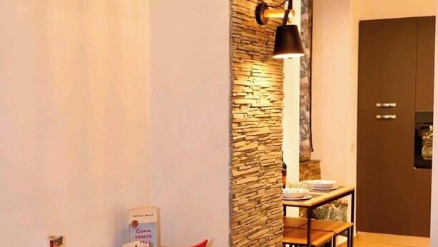 Une cuisine moderne avec un plan de travail en bois, une chaise rouge et un mur d’accent en pierre.