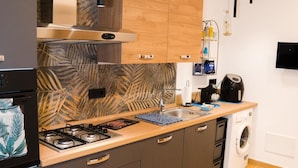 Une cuisine moderne avec des meubles de couleur sombre, une cuisinière à gaz, un four encastré, un lave-linge et un plan de travail en bois.