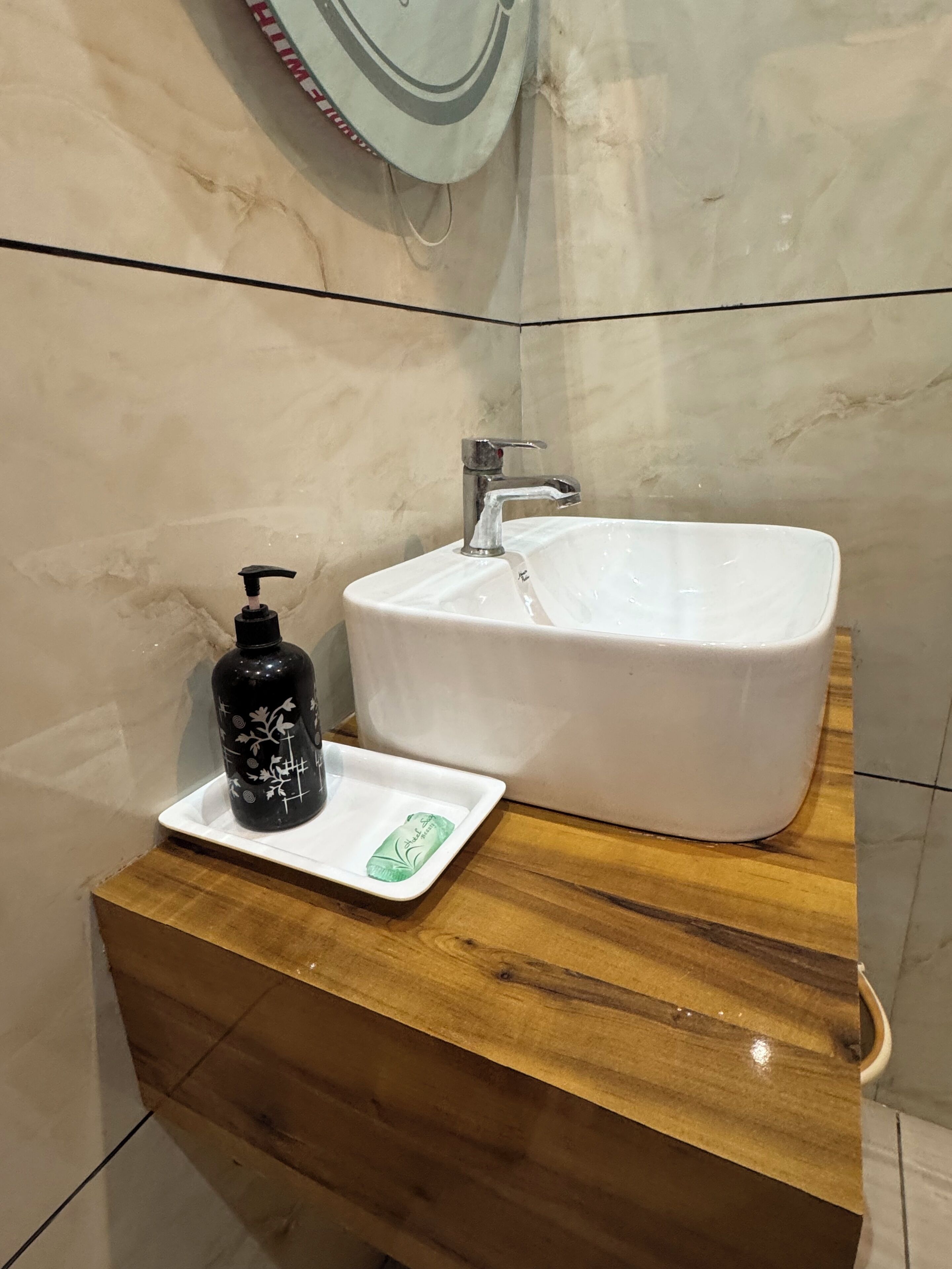 Un baño con un lavamanos blanco, un dispensador de jabón negro y una pastilla de jabón verde sobre una bandeja blanca.