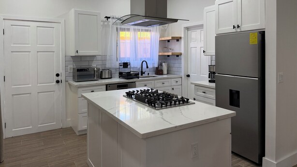 A modern kitchen with white cabinetry, a central island with a gas stove, a stainless steel refrigerator, and a microwave.