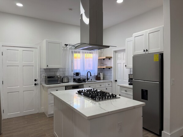 A modern kitchen with white cabinetry, a central island with a gas stove, a stainless steel refrigerator, and a microwave.