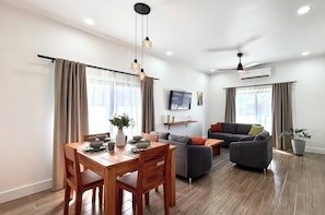Ein modernes Wohnzimmer mit einer Couch, einem Esstisch und Stühlen. Es gibt einen Deckenventilator und eine Klimaanlage.