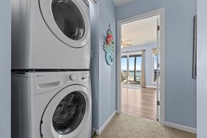 A laundry area with two stacked washing machines, a decorative seahorse wall art, and a view of a balcony with a ceiling fan. - Beach Mountain #211 - 4 BR Oceanfront Surf City Townhome (Surf City)