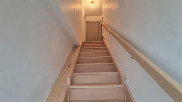 Un escalier en bois, doté d’une rampe, mène à une porte située en haut.