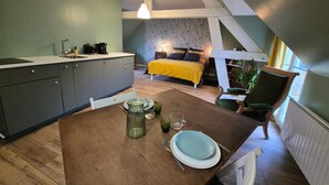 Une cuisine compacte avec un coin repas, un lit recouvert d’une housse de couette jaune et un escalier menant à un niveau supérieur.