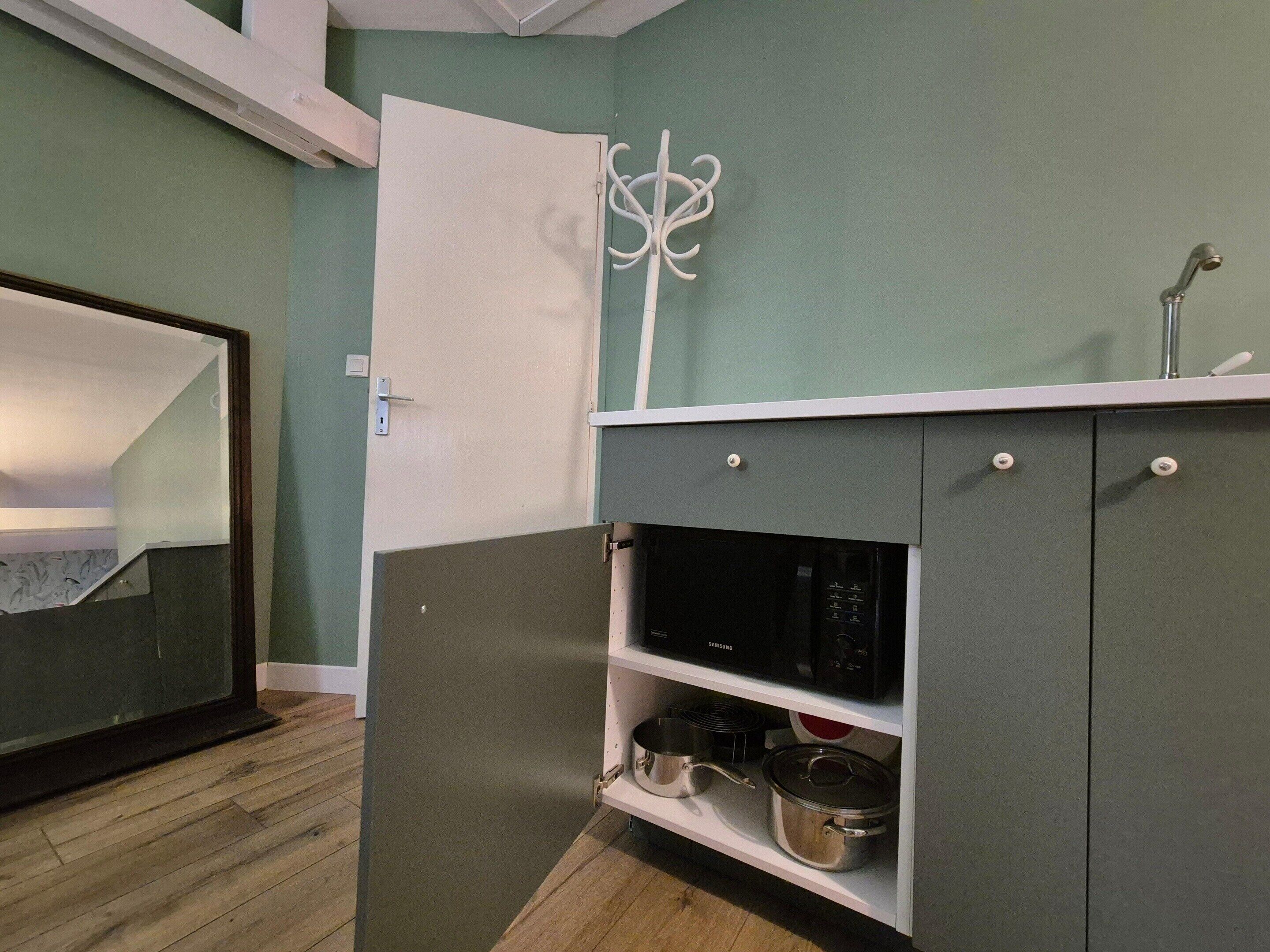 A kitchenette with a microwave, stove, and pots on shelves.