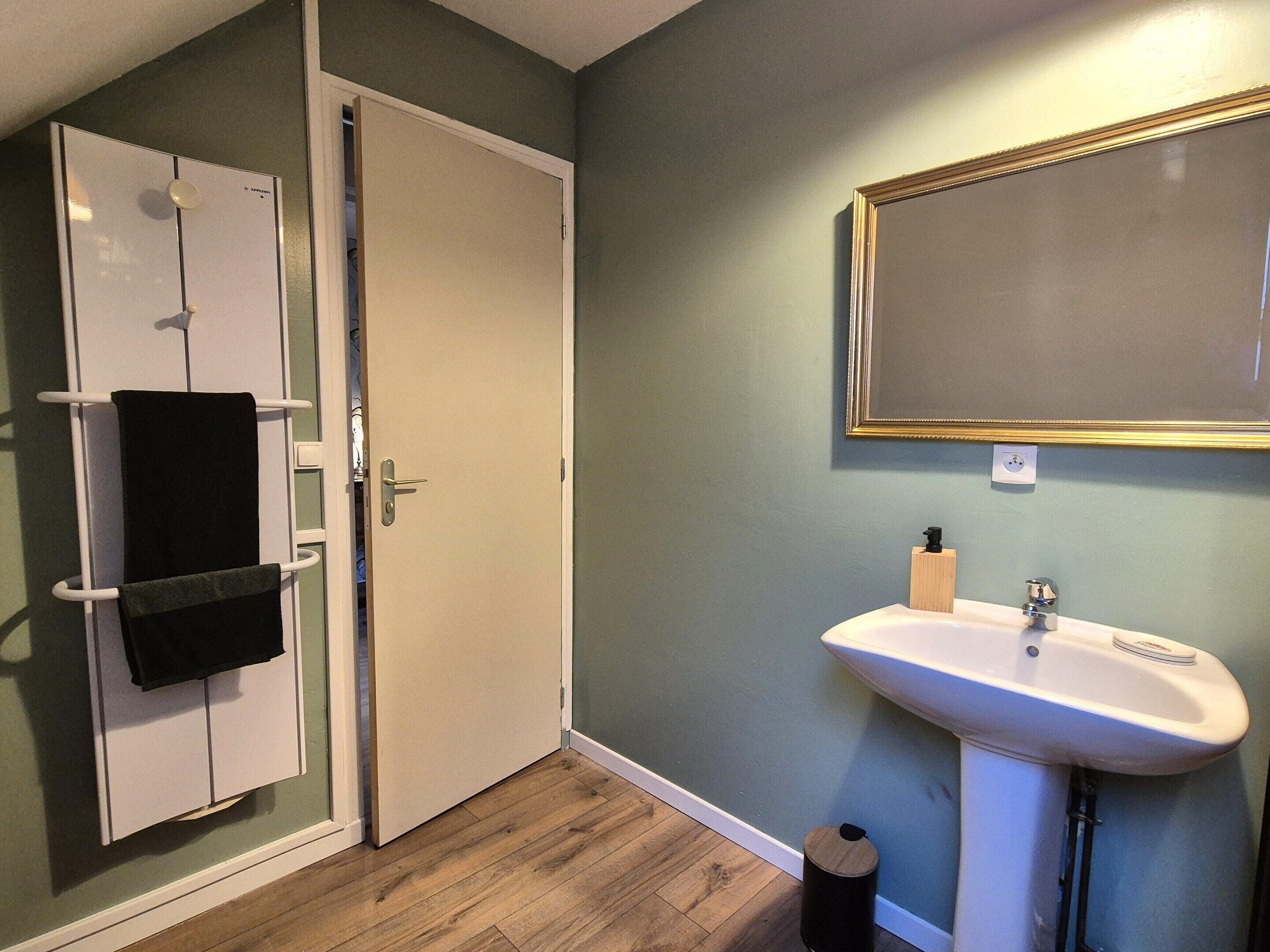 Un baño con lavamanos blanco, espejo y toallero.