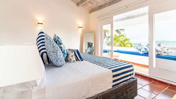 Ein Schlafzimmer mit Bett, Kissen, einem Nachttisch und einem großen Fenster mit Blick aufs Meer.