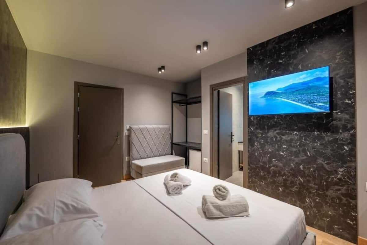Una habitación de hotel moderna con una cama, un televisor instalado en una pared de mármol y vistas a un paisaje costero.