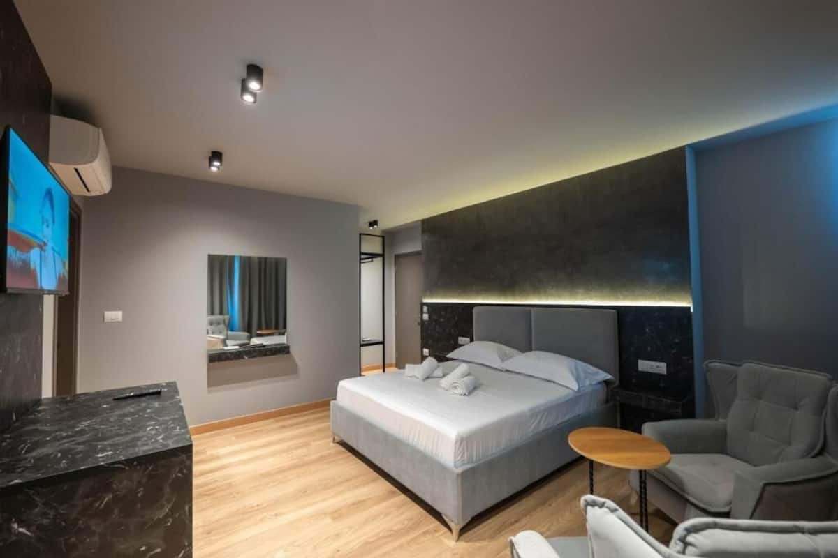 Un dormitorio moderno con una cama grande, una mesita pequeña y un televisor montado en la pared.